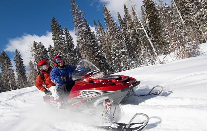 Two people riding a snowmobile through snow